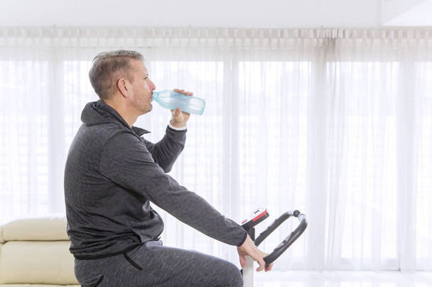 Mature man drinking water on a spin bike - Photo, image