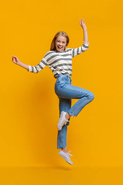 Θετική όμορφη έφηβη κοπέλα που πηδάει στον αέρα με τα χέρια ψηλά - Φωτογραφία, εικόνα