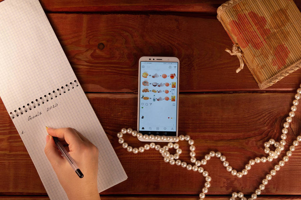 Bolígrafo de mano femenino en bloc de notas abierto. Mujer escribe metas para el nuevo año 2020. Smartphone y collar de perlas en mesa de madera. Concepto de fijar el objetivo en la pérdida de peso, la belleza y la alimentación saludable
. - Foto, imagen