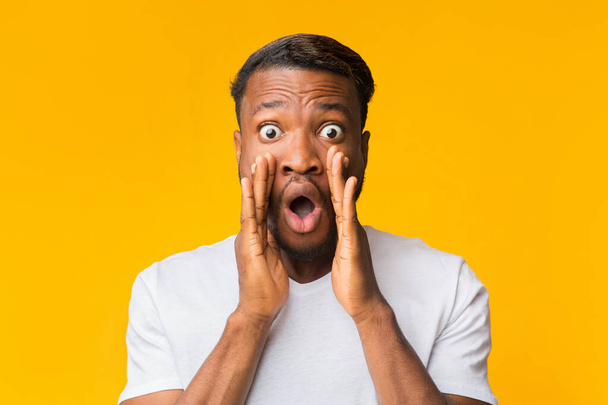 Surpreendido afro homem gritando segurando as mãos perto da boca, fundo amarelo
 - Foto, Imagem