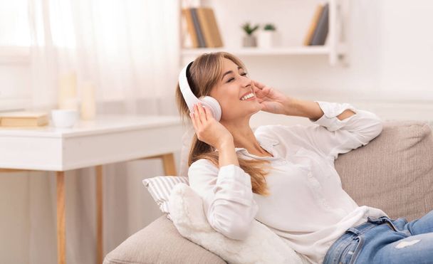 Κυρία στα ακουστικά ακούγοντας μουσική ξαπλωμένη στον καναπέ στο σπίτι - Φωτογραφία, εικόνα