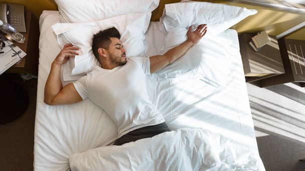 Jongeman slaapt in bed, verblijft in hotel - Foto, afbeelding