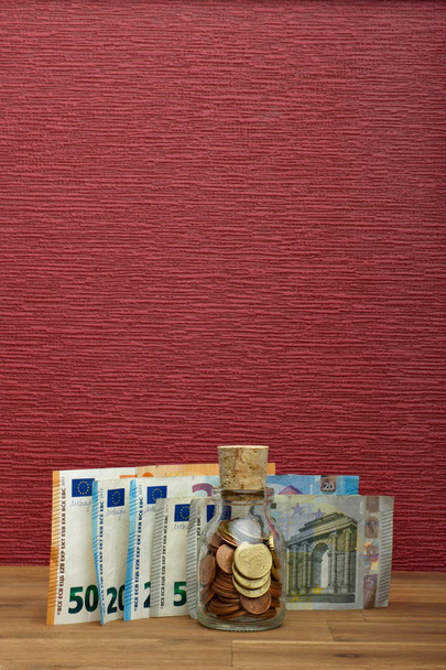 Pièces en euros et billet sur fond rouge bordeaux dans une boîte à monnaie
 - Photo, image