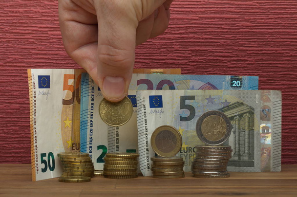 Χέρι κατέχει κέρματα ευρώ και το νομοσχέδιο για το μπορντό κόκκινο φόντο - Φωτογραφία, εικόνα