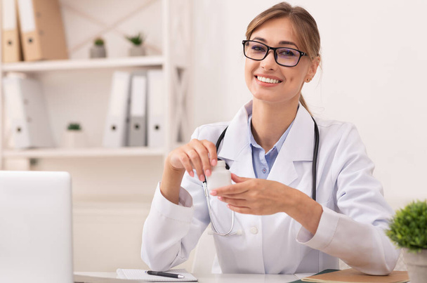 Sorridente medico donna holding prescrizione farmaco vaso seduta in ufficio
 - Foto, immagini