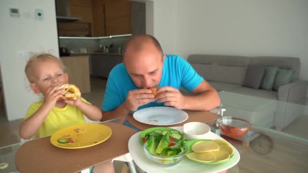 Man and boy with hamburgers - teaching unhealthy diet by example concept - Video, Çekim