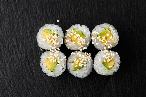 Maki Sushi Rolls with cucumber or avocado on black stone on dark background. Sushi menu. Japanese food. Closeup of delicious japanese food with sushi roll. Horizontal photo - Foto, Imagen