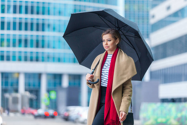 Rain. Outdoors lifestyle fashion portrait of stunning brunette girl. Walking on the city street. Going shopping. Wearing stylish white fitted coat, red neckscarf, black umbrella cane. Business woman. - Fotoğraf, Görsel