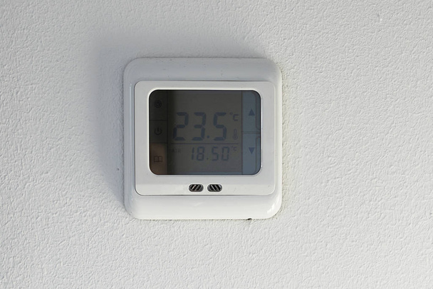 Pantalla montada en la pared que muestra la temperatura del aire interior y exterior y la calefacción. Domótica inteligente: pantalla de temperatura montada en la pared en un termostato digital. Pantalla digital de control climático en una pared blanca
. - Foto, Imagen