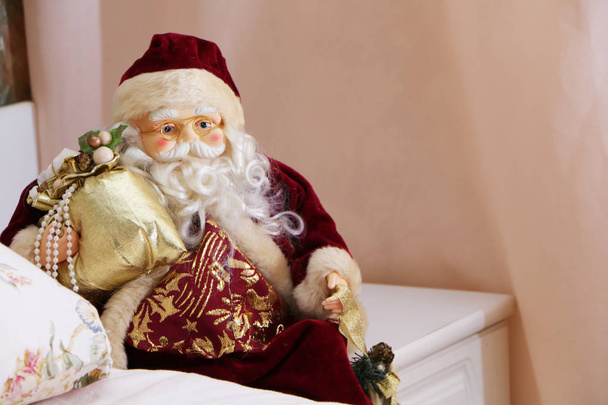 Τα Χριστούγεννα, ο Άγιος Βασίλης κάθεται με ένα δώρο κοντά στο κρεβάτι δίπλα στο  - Φωτογραφία, εικόνα