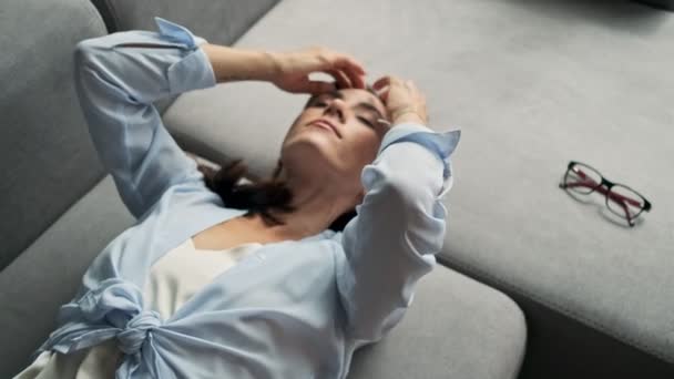 Top view of attractive calm young business woman resting with closed eyes and fixing her hair with hands while lying on sofa at home - Séquence, vidéo