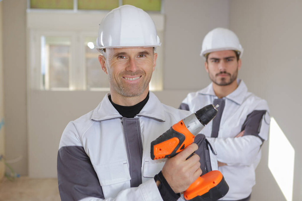 group of smiling builders in hardhats with electric drill indoors - Foto, Imagen