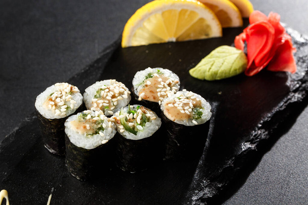 Maki Sushi Rolls with wakame and nut sauce on black stone on dark background. Sushi menu. Japanese food. Closeup of delicious japanese food with sushi roll. Horizontal photo - Foto, imagen