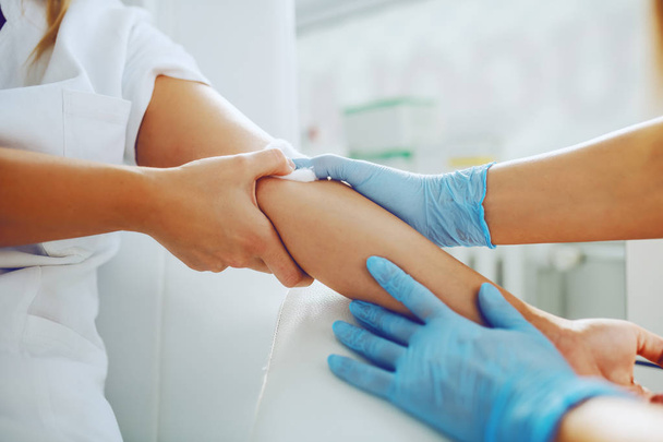Primer plano del asistente de laboratorio que coloca algodón absorbente en el brazo del paciente después de tomar una muestra de sangre
. - Foto, imagen