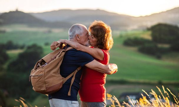 Sırt çantalı yaşlı turistler doğa yürüyüşü yapıyor, öpüşüyorlar.. - Fotoğraf, Görsel