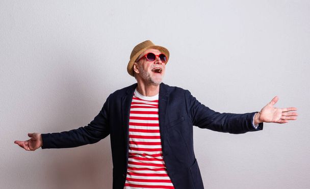 Portrait of a senior man with red sunglasses in a studio, arms stretched. - Foto, Bild