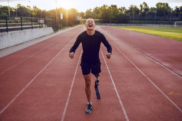 Sportos jóképű kaukázusi fogyatékos férfi mesterséges lábbal áll a versenypályán, és motiválja magát a futásra. - Fotó, kép