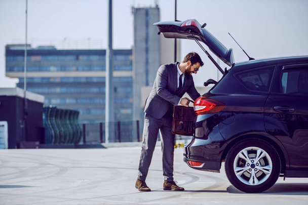 Full length of handsome caucasian bearded businessman with sunglasses taking his leather bag from trunk. - Foto, Bild