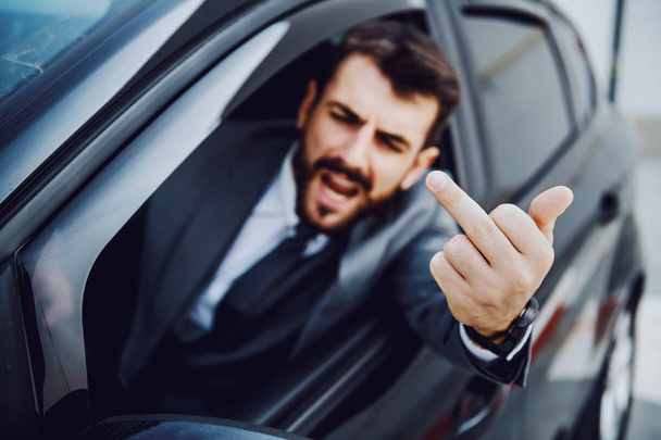 Rude caucasian bearded businessman driving his car and showing middle finger to other drivers. - Photo, Image