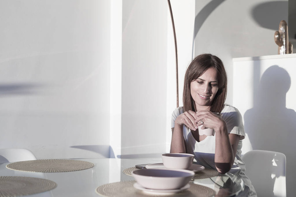 Hosszú hajú nő ül a nappaliban, miközben kezében egy csésze teát - Fotó, kép