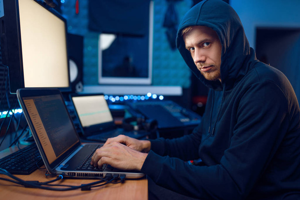 Haker w kapturze siedzi przy laptopie, hakuje informacje. Internetowy szpieg, programista próbujący zhakować zaszyfrowaną sieć - Zdjęcie, obraz