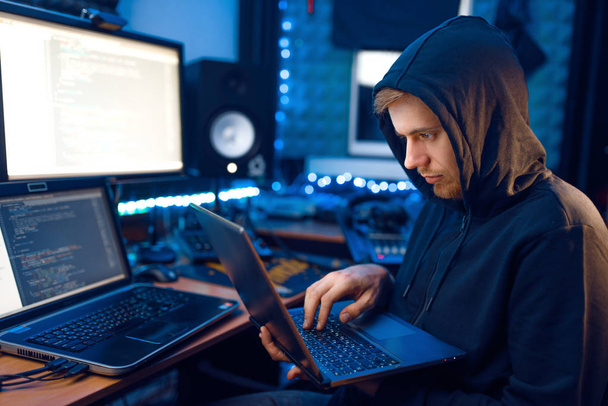 Хакер в капюшоне показывает большие пальцы на своем рабочем месте с ноутбуком и компьютером, паролем или взломом учетной записи. Интернет-шпион, криминальный образ жизни
 - Фото, изображение