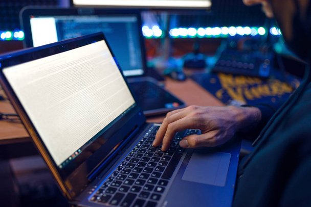 Hacker mit Kapuze zeigt Daumen hoch an seinem Arbeitsplatz mit Laptop und PC, Passwort oder Account-Hacking. Internet-Spion, krimineller Lebensstil, Risiko-Job, Netzwerk-Verbrecher - Foto, Bild
