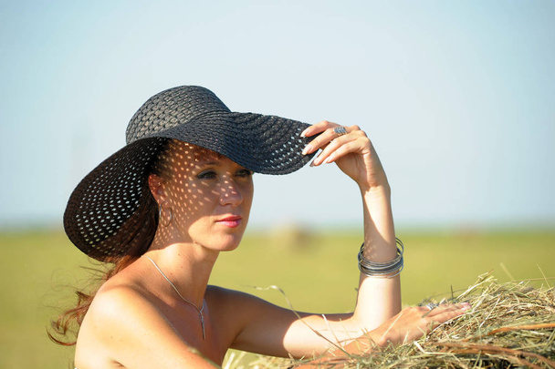 girl in a black dress in the summer in a field near a haystack p - Foto, Bild