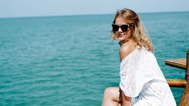Young woman near sea in white dress and sunglasses on azure background - Photo, Image