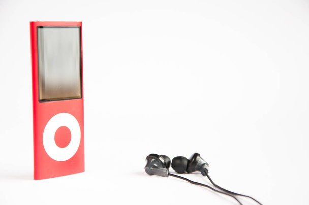 A red iPod and black vacuum headphones are on the table. On white background. - Photo, Image