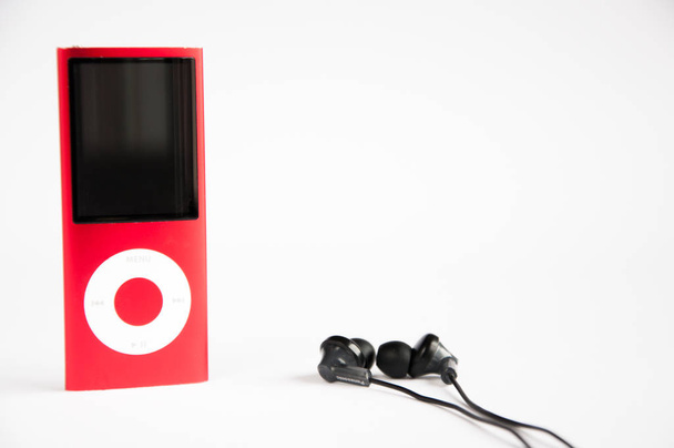 Um iPod vermelho e auscultadores a vácuo pretos estão sobre a mesa. No fundo branco
. - Foto, Imagem