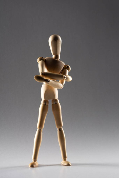 A vertical shot of a wooden pose doll with crossed arms standing in the shade on a white background - Photo, Image