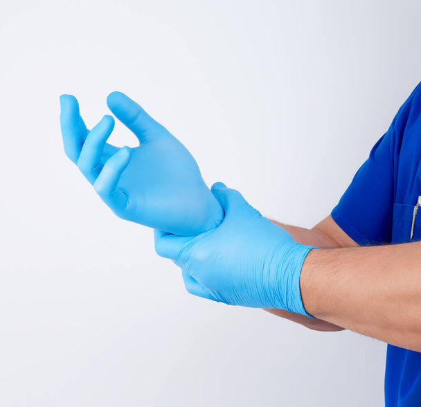 мужчина в синей форме надевает на руки белый стерильный поздно
 - Фото, изображение