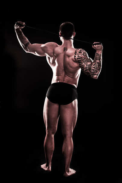 rear view. A muscular man performs exercises using a resistance band - Photo, Image