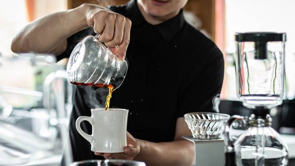 A person pouring coffee into a cup in a coffee shop - Photo, Image