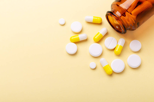 Multicolor tablets and pills capsules from glass bottle on yellow background Close-up - Photo, Image