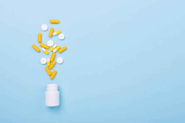 Multicolor tablets and pills capsules from plastic bottle on blue background - Fotó, kép