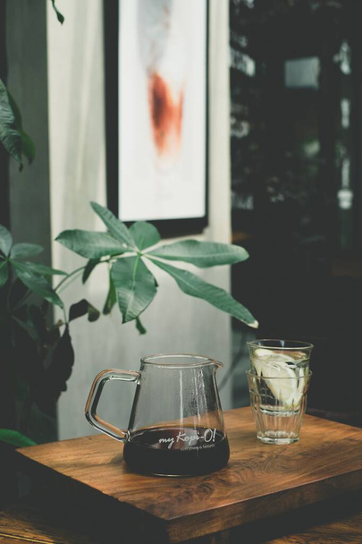 A vertical shot of a teapot and a glass on a wooden table - Foto, Bild