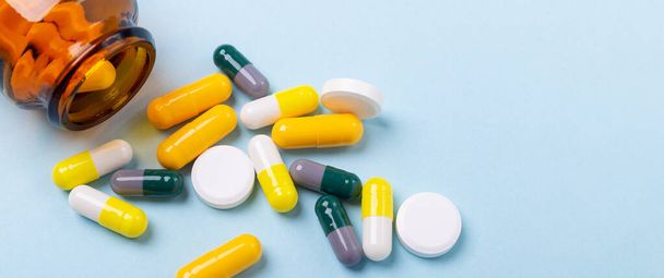 Multicolor tablets and pills capsules from glass bottle on blue background Horizontal banner - Foto, Imagem