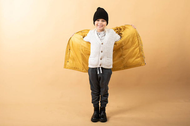 kleine jongen in geel jasje, trui en hoed op gele achtergrond. winter - Foto, afbeelding