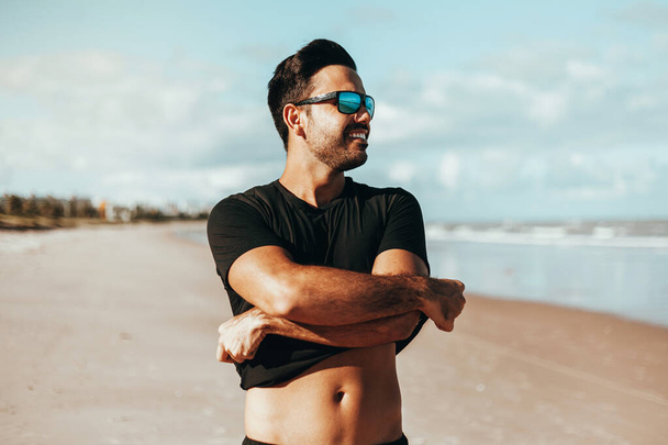Summer time. Smiling man taking off his shirt at the beach - Photo, image