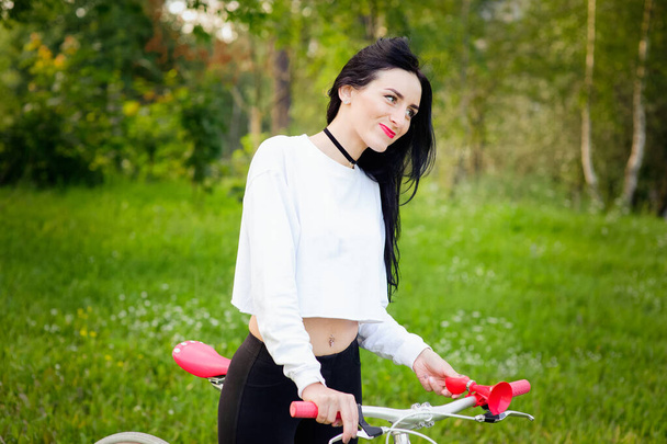 Kaunis tyttö poseeraa polkupyörällä. Valkoinen ja punainen pyörä. kävellä luonnossa. terveellistä elämäntapaa. viikonloppuna luonnossa Muotokuva onnellinen kaunis tyttö valkoinen T-paita. kirjoituspaikka
 - Valokuva, kuva