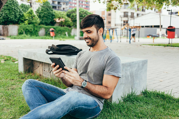 Young man reading e-book in the park - Zdjęcie, obraz