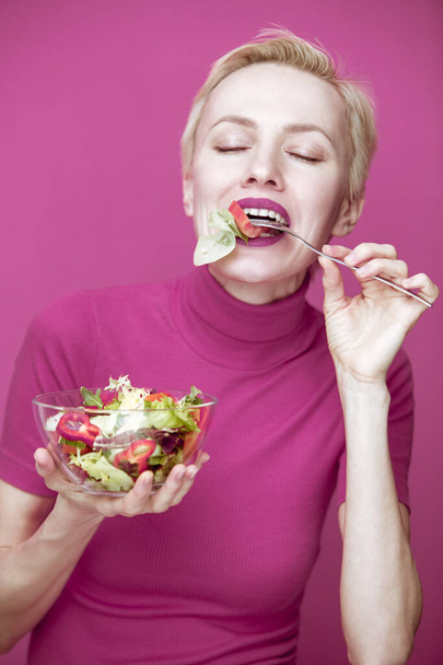  Beautiful caucasian woman eating salad over pink purple background. studio shot - Foto, immagini