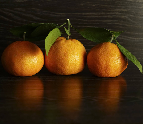 3 three Fresh, ripe tangerines with leaves on a black stone surface.  - Photo, image