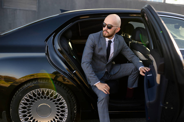Business man in suit opening black car door - Photo, image