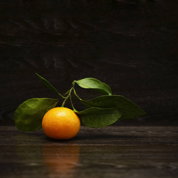 Fresh, ripe tangerine  with leaves on a black stone surface. Orange and green. Seasonal citrus fruit - 写真・画像