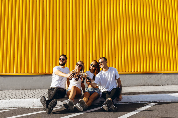 A group of young friends hang out in the city sitting on the asphalt at the yellow wall - 写真・画像