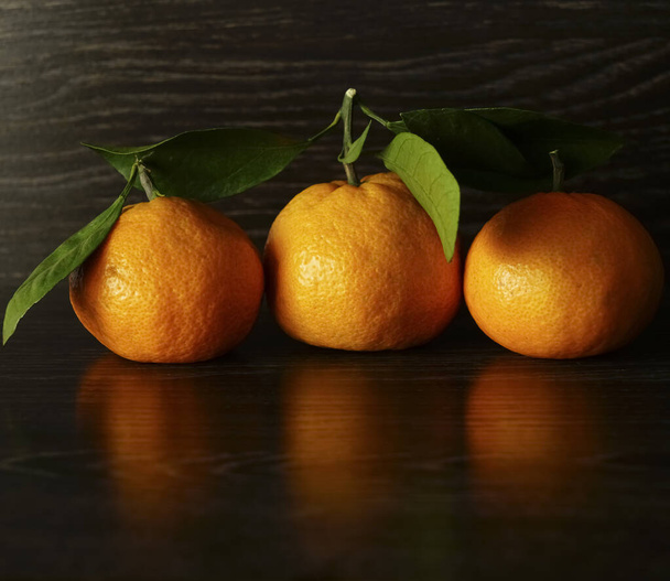 3 three Fresh, ripe tangerines with leaves on a black stone surface.  - Foto, immagini