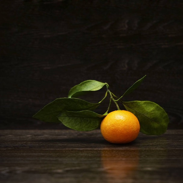 Fresh, ripe tangerine  with leaves on a black stone surface. Orange and green. Seasonal citrus fruit - Фото, зображення